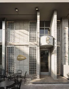 A modern building exterior with a large glass wall and a patio area featuring various-sized chairs in different positions, inviting a comfortable outdoor seating experience