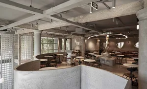Open modern restaurant interior with a concrete finish, multiple tables, and comfortable seating for guests