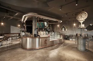 A modern coffee shop interior with a stainless steel counter, displaying various drinks and food items, in a warm and inviting atmosphere