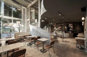 A modern restaurant interior with a spiral staircase, seating areas, and potted plants, creating an inviting atmosphere