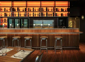 Warm and inviting bar area with a wooden countertop, stools, and bottles, featuring a rustic charm