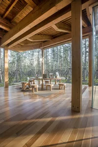 Open living area with a large wooden table, benches, and comfortable seating, creating a cozy atmosphere with wood elements and furnishings
