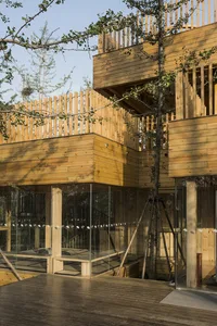 A wooden house with multiple levels, a deck, and glass elements, surrounded by trees and a bird, conveying a warm and inviting atmosphere