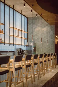 Modern bar area with a long counter and stools, surrounded by bottles and ambient lighting