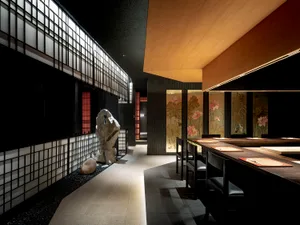 A modern Asian restaurant with tile flooring, tables, chairs, and potted plants, complemented by artwork on the walls