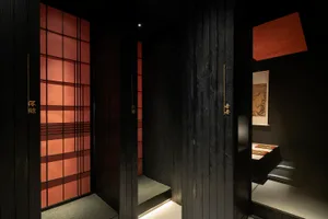 A black wooden door with gold accents in an Asian-style bathroom with a red tiled wall