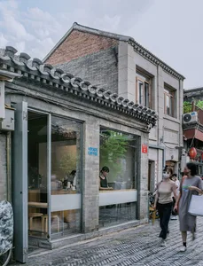 A bustling urban coffee shop with a brick facade, natural light, and people walking by on the sidewalk