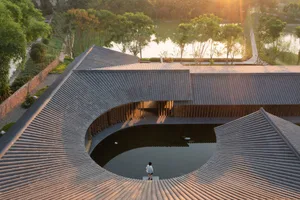 A serene architectural scene featuring a circular structure surrounded by trees and water, with a person standing on a platform within the structure
