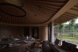 Cozy restaurant interior with a dining area and living room featuring a round table, chairs, couch, and bench, with wine glasses and a warm atmosphere