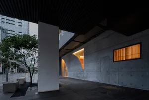 A modern building with a concrete facade, featuring a large window and nighttime lighting