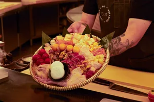 A man holds a large woven basket filled with a variety of fruits, vegetables, and meats in a warm and inviting atmosphere