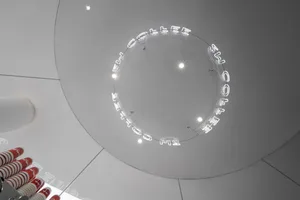 A modern interior space with a large circular opening in the ceiling, surrounded by a ring of lights, and minimalist design elements