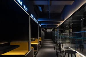 A modern restaurant or bar area with a long hallway featuring benches and chairs, overhead lighting, and a welcoming atmosphere
