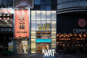 A modern commercial building with a yellow and black facade, featuring a large sign reading WAT, suggesting a restaurant or store