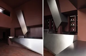 Industrial-style bar with metal counter, books, and wine glasses, set against a background of bottles and possibly a reading area