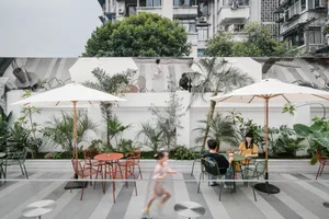 Outdoor dining area with tables, chairs, umbrellas, and greenery, featuring a casual and inviting atmosphere