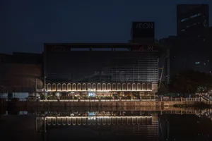 A modern building with a large glass structure and reflective surface, lit up at night, surrounded by potted plants and a dark sky
