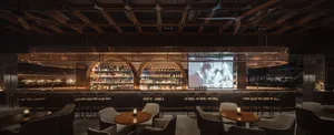 A cozy bar area with a wooden counter, chairs, and a mounted TV, surrounded by bottles and inviting atmosphere