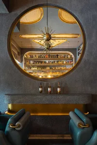 A cozy bar area with a large mirror behind the counter, bottles, and chairs, creating a warm and inviting atmosphere