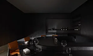 A dark and moody restaurant dining area with a table and chairs, wine glasses, and scattered bottles