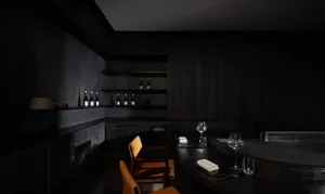 Dark and intimate bar area with a black countertop, dining table, chairs, wine glasses, and bottles