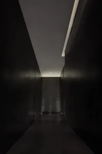 Dark hallway with black tile floor, stone walls, and ceiling lights