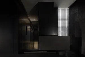 Dark modern kitchen dining space with a black countertop, a dining table, and a chair, surrounded by walls and minimal decor