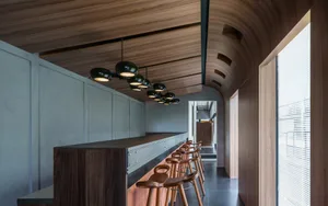 A well-lit restaurant interior with wooden floors and walls, featuring a dining table and various chairs, creating a warm and inviting atmosphere