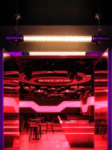 A modern bar area with a red glow, a counter, stools, and chairs, creating a lively ambiance