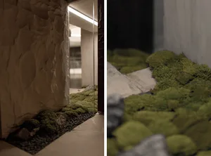 A serene indoor space with lush greenery, natural stone walls, and a large rock centerpiece, surrounded by doorway and interior design elements