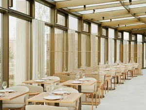 A well-lit restaurant with wooden floors and dining tables, featuring rows of chairs and a warm atmosphere