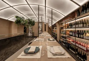 A dining room with a long wooden table set with wine glasses, plates, and napkins, surrounded by chairs, with a potted plant adding greenery to the space