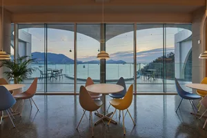 Dining area with a large window offering an ocean view, featuring a white table and various chairs with a yellow seat in a modern and inviting atmosphere