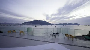 A patio area with chairs and dining tables arranged around a glass wall overlooking the ocean, creating a relaxing and inviting atmosphere