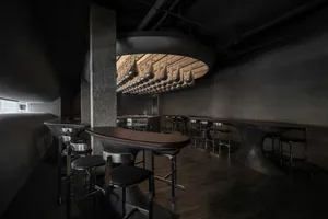 Dark and intimate bar area with a round table, chairs, and bottles, creating a cozy ambiance for patrons