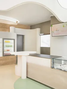 A casual cafe interior with a counter featuring a refrigerator and bottles, cups, and a welcoming atmosphere