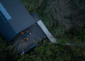 A photo of a house with a wooden exterior, a deck, and stairs leading to a lower level, featuring chairs and dining tables for relaxation and socializing