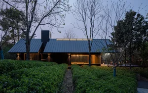 A modern house with a black roof and a green lawn, surrounded by trees, featuring a large window for natural light and a clean, minimalistic design