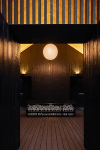 A warm and cozy living dining space with wooden walls, a central bench, and a round light fixture