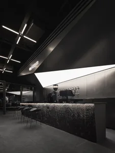 A modern bar area with a black countertop, coffee machine, and two chairs, well-lit by overhead lights