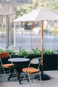 A well-lit outdoor patio with two chairs under a white umbrella and a dining table in the middle, creating a comfortable seating arrangement