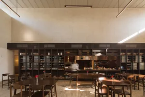 Modern restaurant interior with wooden tables and chairs, multiple dining tables with chairs and benches, and a warm atmosphere
