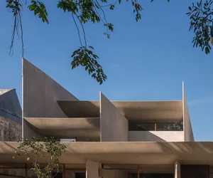 A modern building with concrete walls and a glass facade, set against a backdrop of trees and an urban environment
