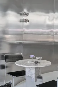 A modern dining space with a round marble table, two chairs, and a vase of flowers, set in a well-lit room