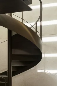 A modern metal staircase near a window, illuminated by natural light, with a sense of depth and complexity within the structure