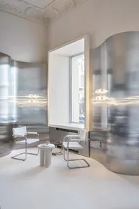 A modern living space with two white chairs and a dining table near a large window, featuring clean lines and simple shapes, and well-lit by natural sunlight