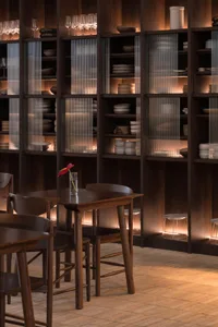 A restaurant interior with wooden floors and walls, featuring multiple dining tables, chairs, and wine glasses, creating a warm and inviting atmosphere