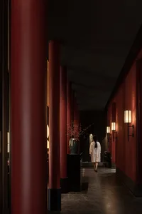 A woman walks down a red-walled hallway with vases and a potted plant, creating a warm and inviting atmosphere
