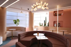 Modern restaurant interior with a circular dining area, pink accent wall, and a large chandelier, surrounded by potted plants