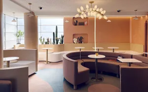 Cozy cafe with a circular seating area, warm-toned walls, and potted plants, illuminated by light fixtures